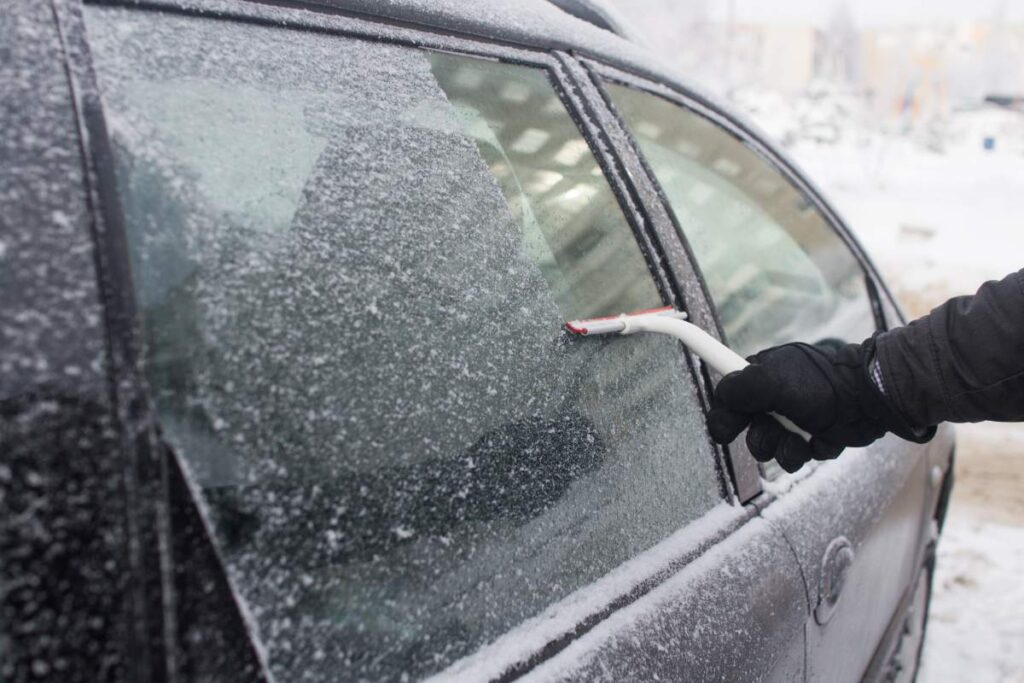 man cleans snow from car window