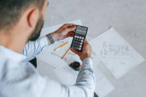 Calculating numbers by using smartphone. Plan is on the floor. The man is making repairs in the apartment