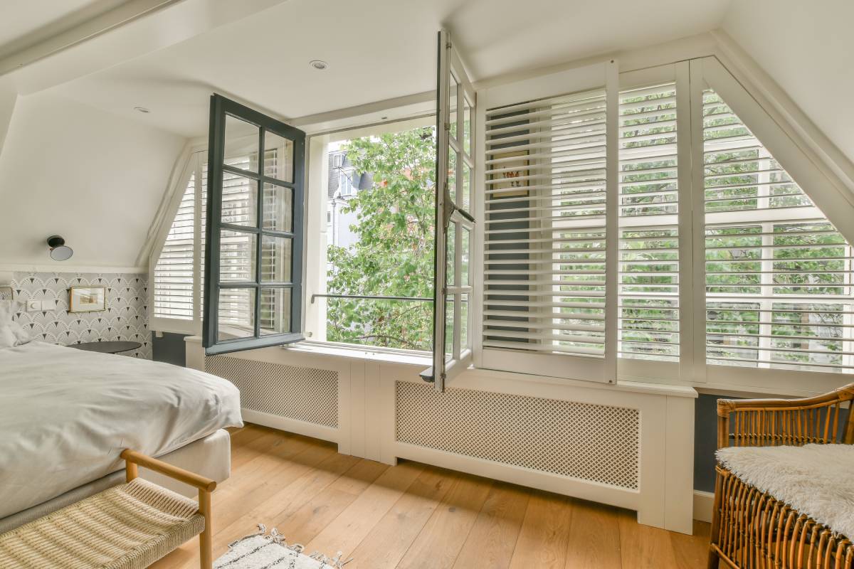 Home interior design of bedroom with bed and wooden wardrobe placed in corner near window in modern apartment