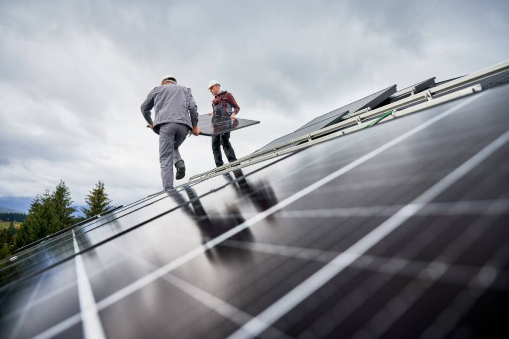 Technicians carrying photovoltaic solar module while installing solar panel system on roof of house