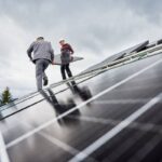 Technicians carrying photovoltaic solar module while installing solar panel system on roof of house