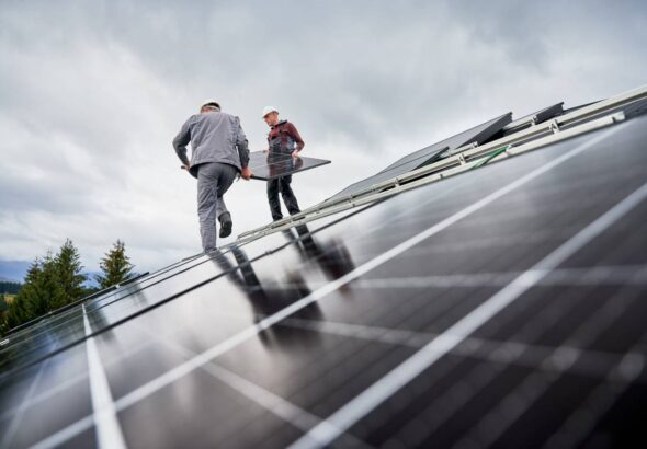 Technicians carrying photovoltaic solar module while installing solar panel system on roof of house