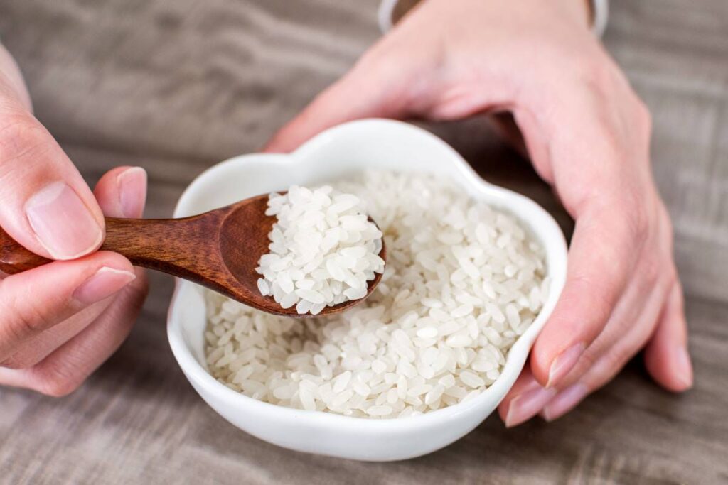 Closeup of hands holding a wooden spoon with rice grains over a bowl