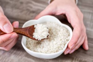 Closeup of hands holding a wooden spoon with rice grains over a bowl