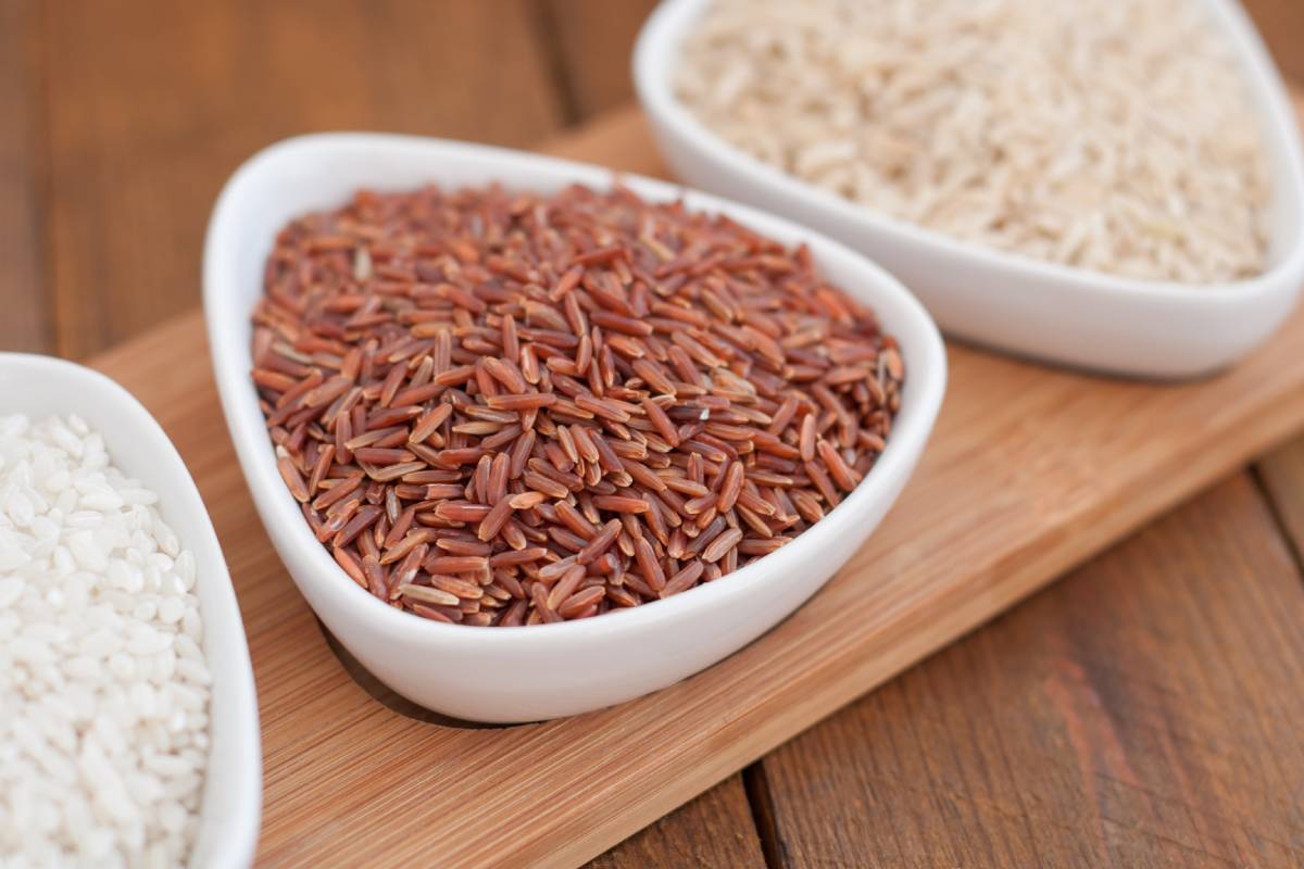 Red rice in a bowl close up on wooden plank