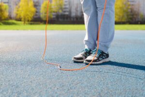 Close-up of woman jumping rope exercising on sports field outdoors on sunny day. Fitness, aerobics and active lifestyle. Low angle view